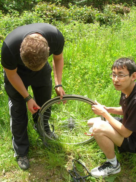 Jiaxin heeft een lekke band. Bleek een poot van een dun nietje te zijn, dat nog in de buitenband stak. Het was een piepklein gaatje. We hadden geen plakkers mee, dus moest er een nieuwe binnenband in. Hele wiel er uit. Zoals hier te zien is fietst Jiaxin zonder versnellingen. Monospeed heet dat. Vindt hij stoerder. Afzien is een gave.